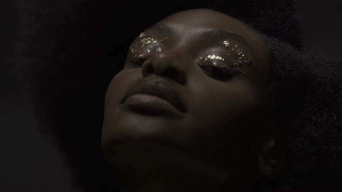 Model with gold leaf on her closed eyes against a dark grey backdrop