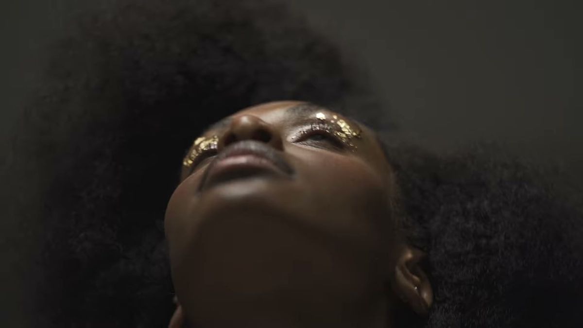 Low-angle portrait of a model with gold leaf on her eyelids, head tilted back, 111SKIN