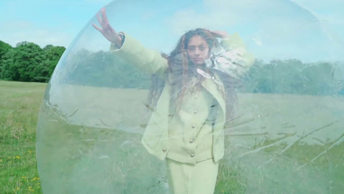 Model in a pale suit inside a clear plastic sphere in a field