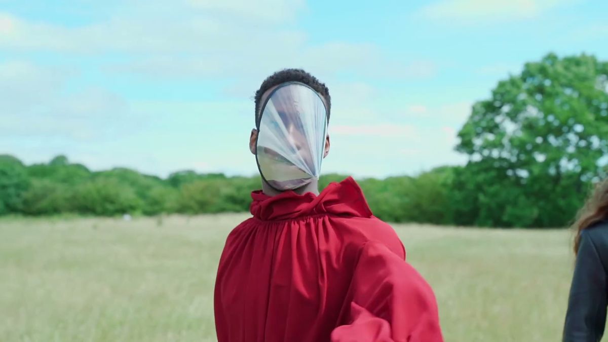 Model in a red cape with a clear plastic face shield in an open field, 1883 Magazine 2 metres distance film