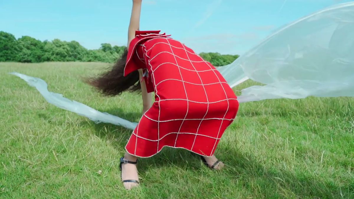 Model in a red check dress moving with a clear plastic sheet trailing behind