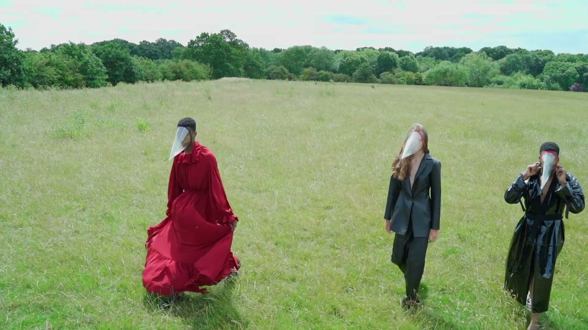 Three masked models walking towards camera across a field