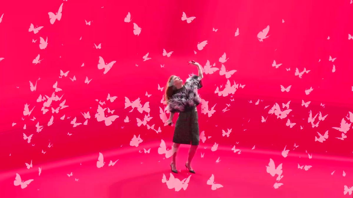 Rose Leslie on a pink set surrounded by butterflies, wide shot
