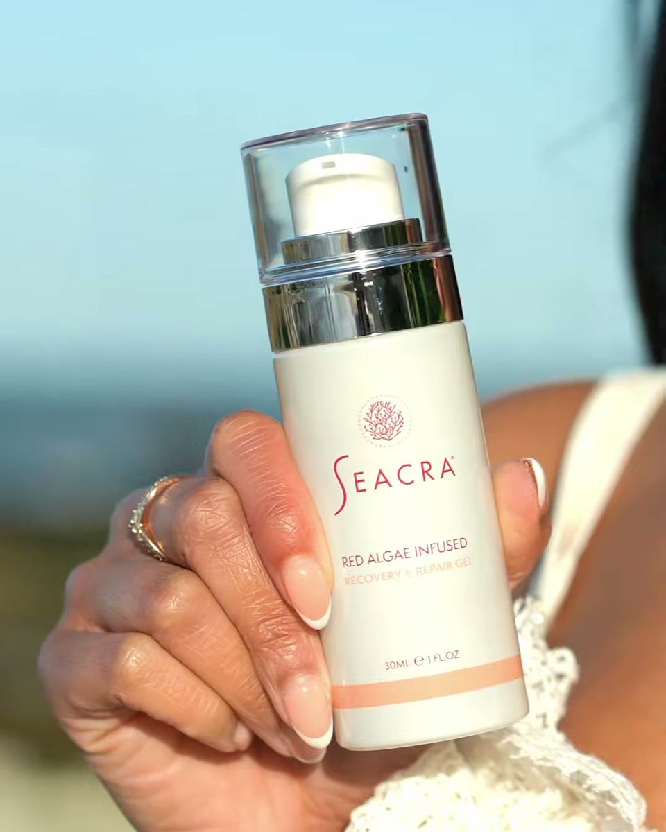 Hand holding a Seacra red algae infused bottle outdoors against the sky