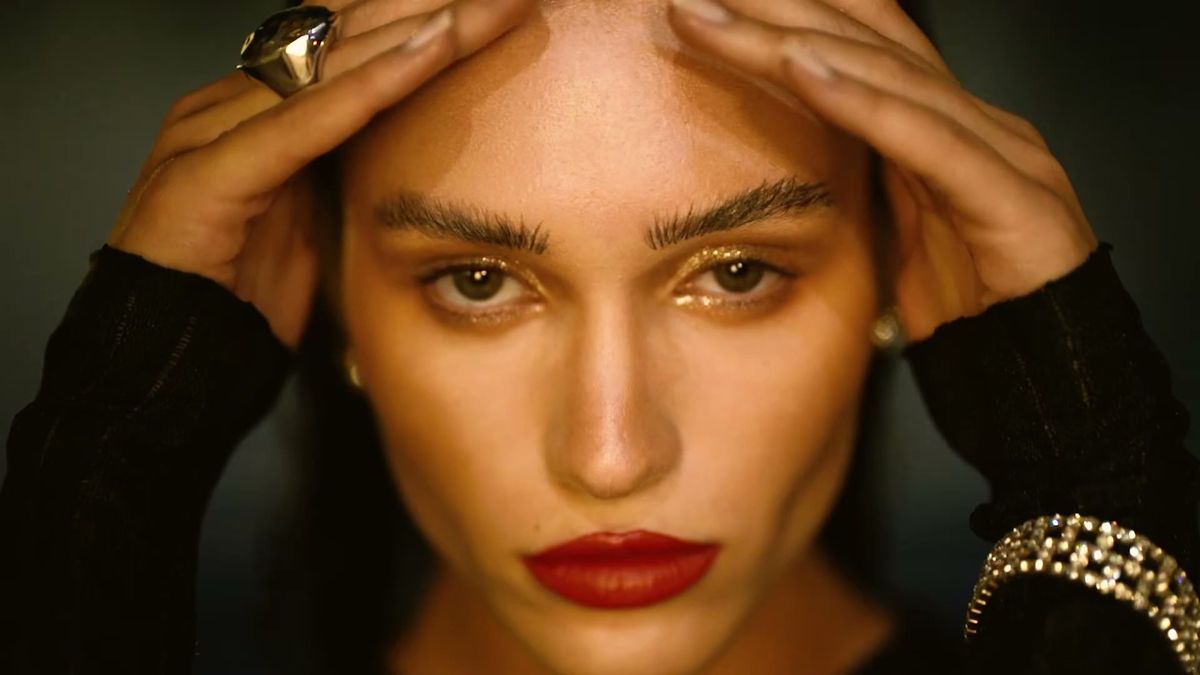 Beauty portrait in warm light, hands on head, red lip and gold bracelet