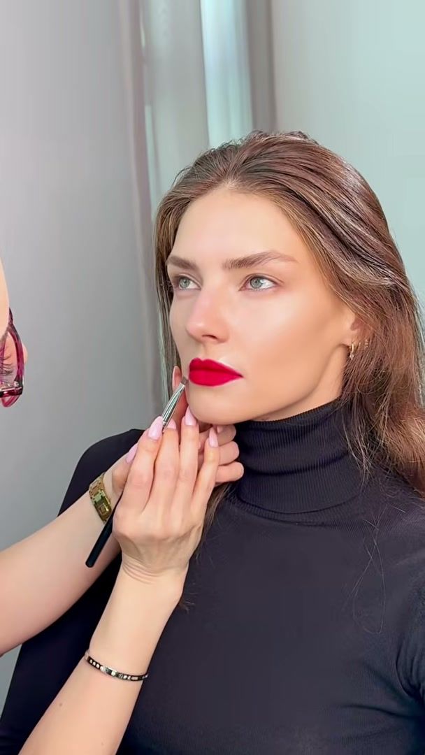 Make-up artist lining a red lip on a model in a black turtleneck, Waterproof beauty editorial