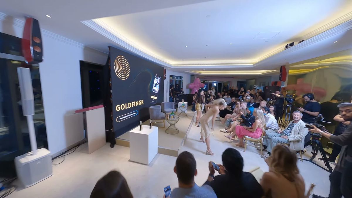 Wide FPV frame of a brand event inside a Dubai tower, a branded screen beside a performance and a seated audience