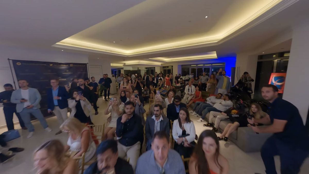 FPV drone frame flying over a packed, seated audience at an indoor event in Dubai