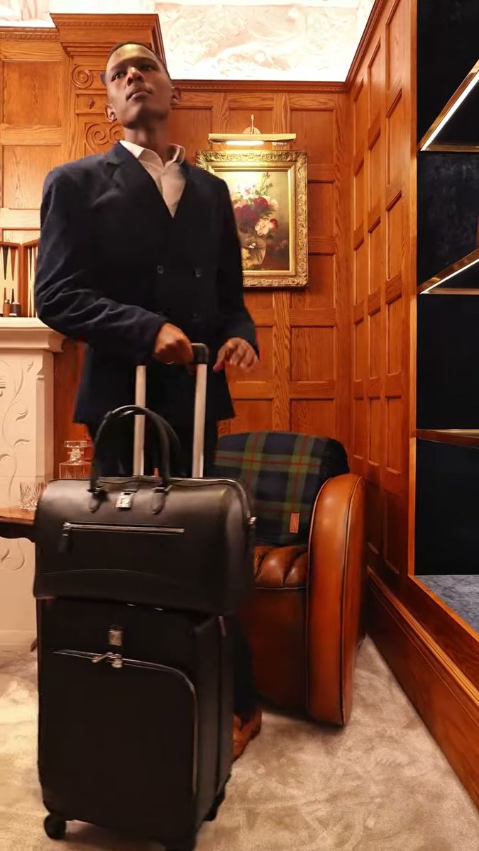 Man in a navy suit with Aspinal of London luggage in a wood-panelled room