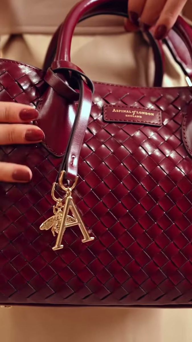 Close-up of a gold letter charm on a burgundy woven leather bag