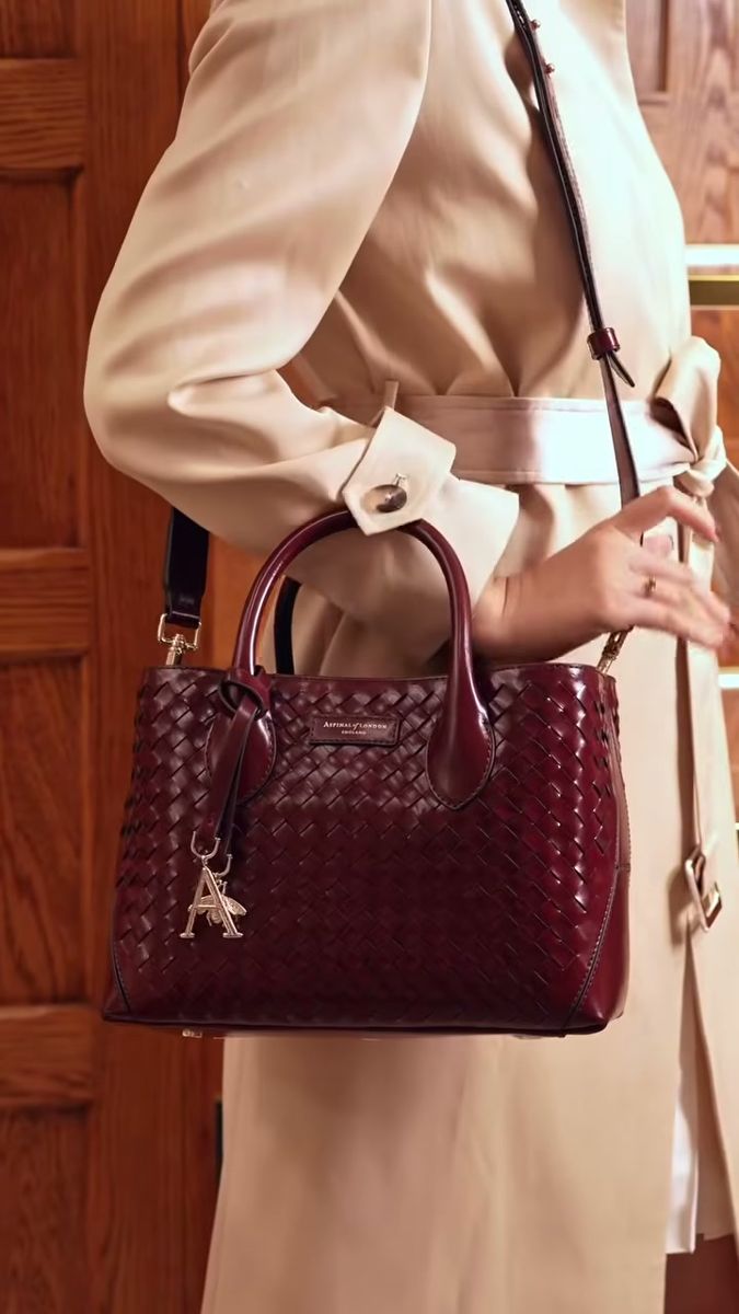 Woman in a camel trench coat carrying a burgundy handbag