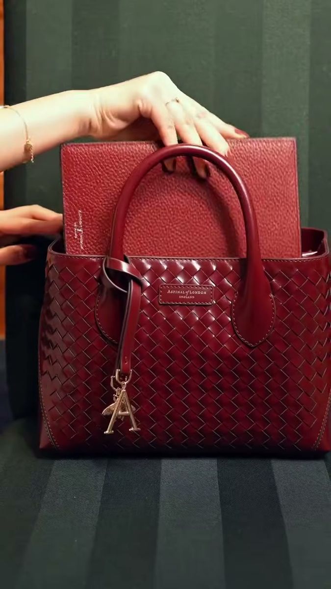 Hand placing a red leather notebook into a burgundy handbag