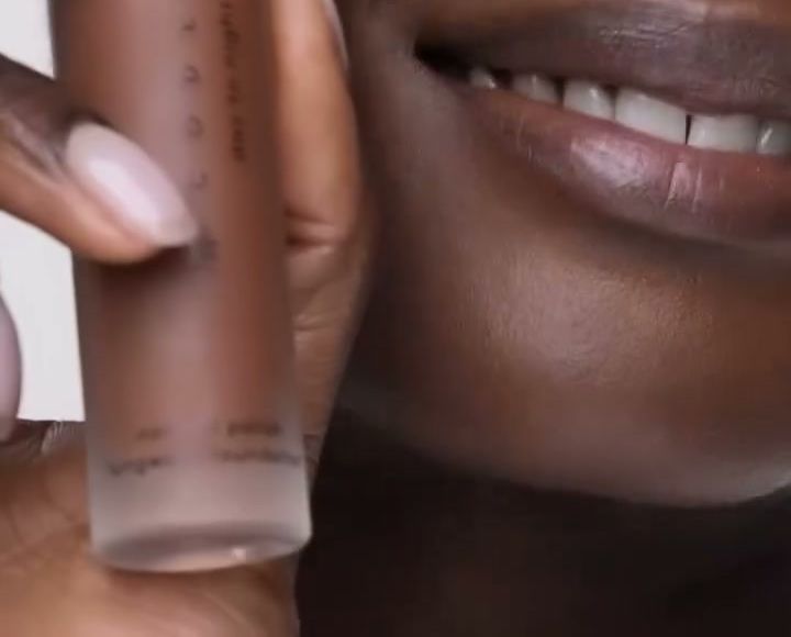 Model with deep skin holding a Code8 Day to Night Foundation bottle beside her smile