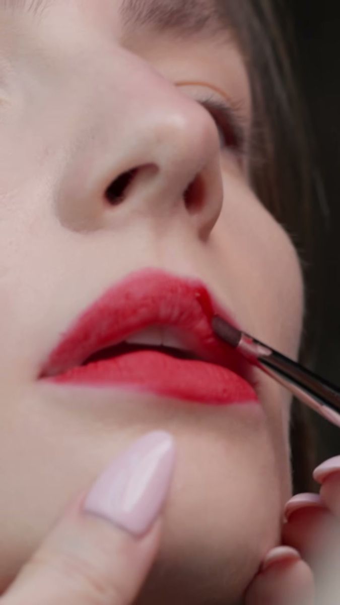 Close-up of a red lip being painted with a brush, real skin texture