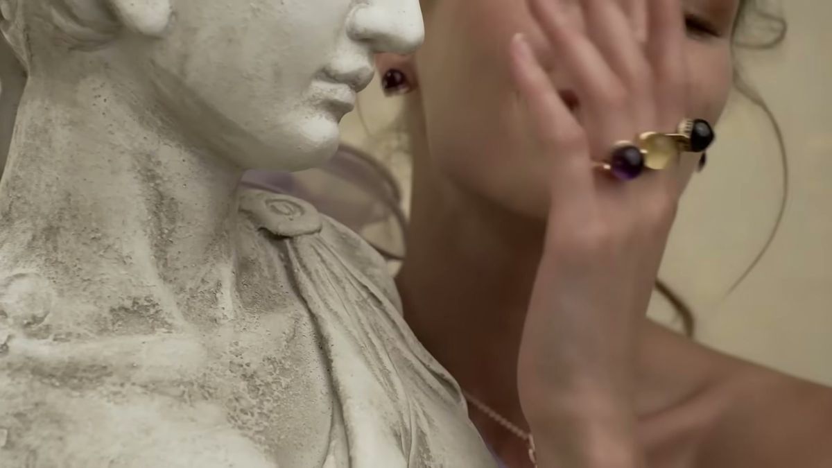Close-up of Damas gemstone rings on a model's hand beside a marble statue