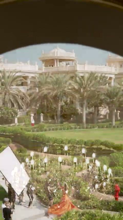 View through an arch onto a palace garden set with a model in an orange gown, Damas x Dome
