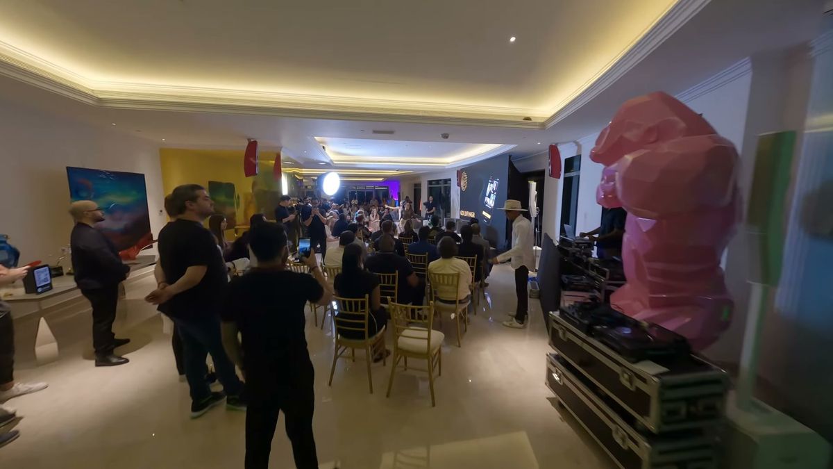 FPV drone flying past a pink sculpture towards a seated audience at an event in a Dubai tower