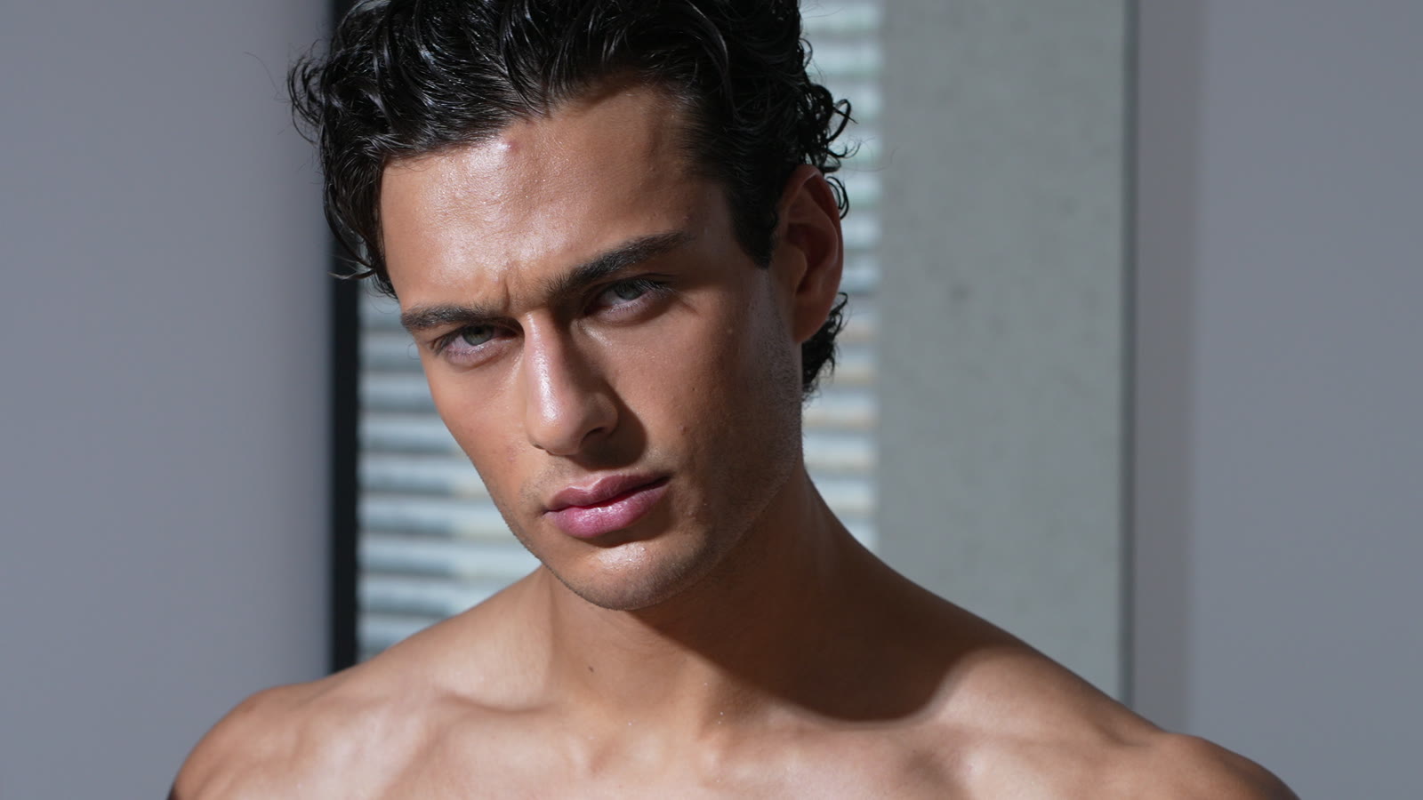 Model with dark curly hair looking into the lens beside window blinds, DRT Bodywear commercial, London