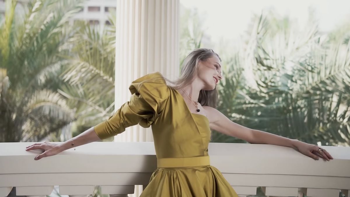 Model in a gold gown leaning on a white balustrade, Damas campaign, Dubai