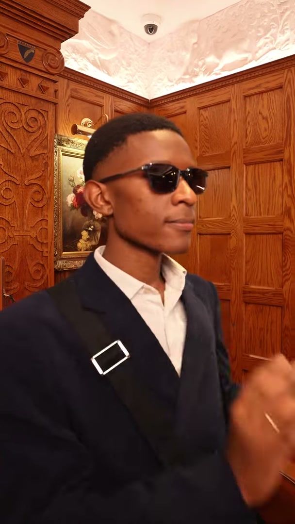 Model in sunglasses wearing an Aspinal of London crossbody bag, panelled room