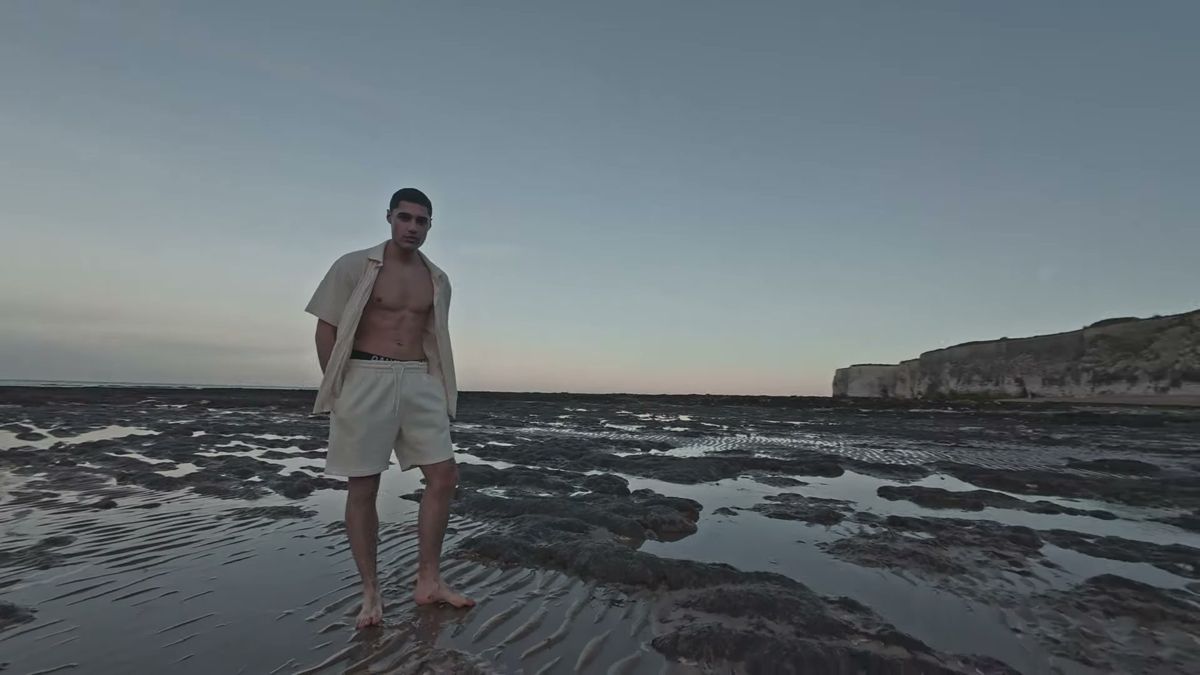 Male model in an open shirt standing on the rock shelf at low tide, Kent coast