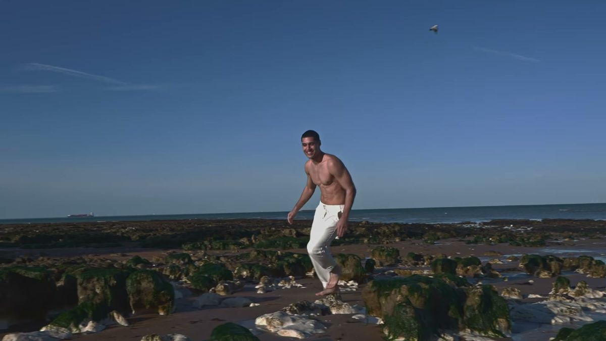 Male model stepping across seaweed rocks on the Kent coast, with the FPV drone in the sky