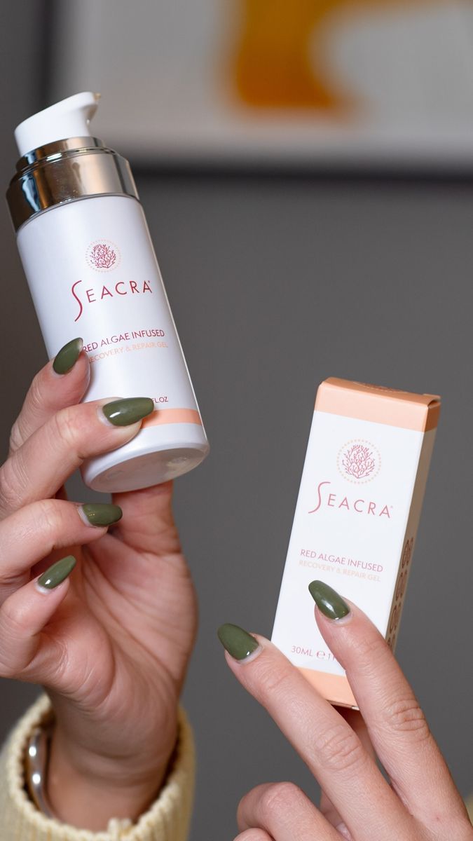 Hand with green nails holding a Seacra bottle next to its box