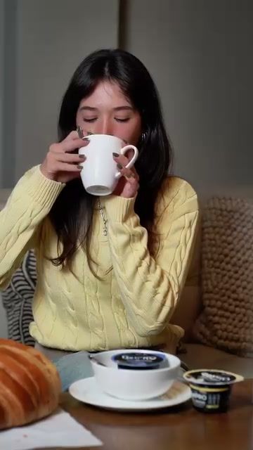 Young woman in a yellow jumper sipping coffee at a cafe table, creator-style routine video