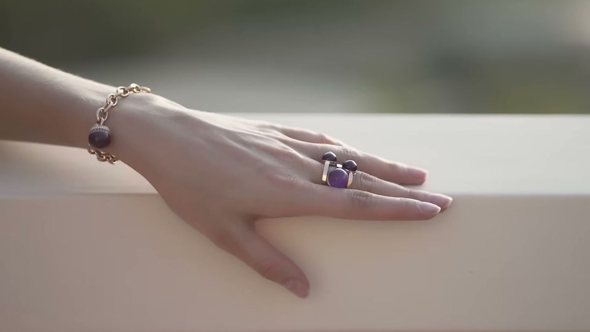 Hand resting on a stone balustrade wearing a gemstone ring and a gold bracelet, from a Damas campaign film