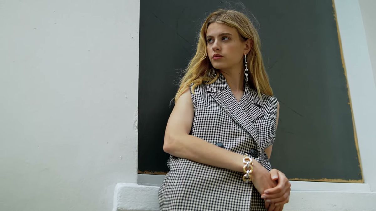 Model in a gingham waistcoat with drop earrings and a chain bracelet, on a Staccato shoot in London