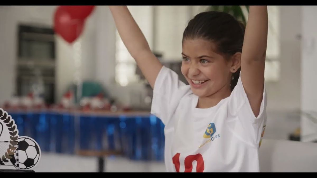 Girl in a football shirt throwing her arms up in celebration during the KickOff board game commercial