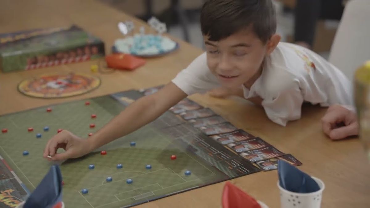 Boy leaning over the KickOff football board game moving red and blue pieces on the pitch
