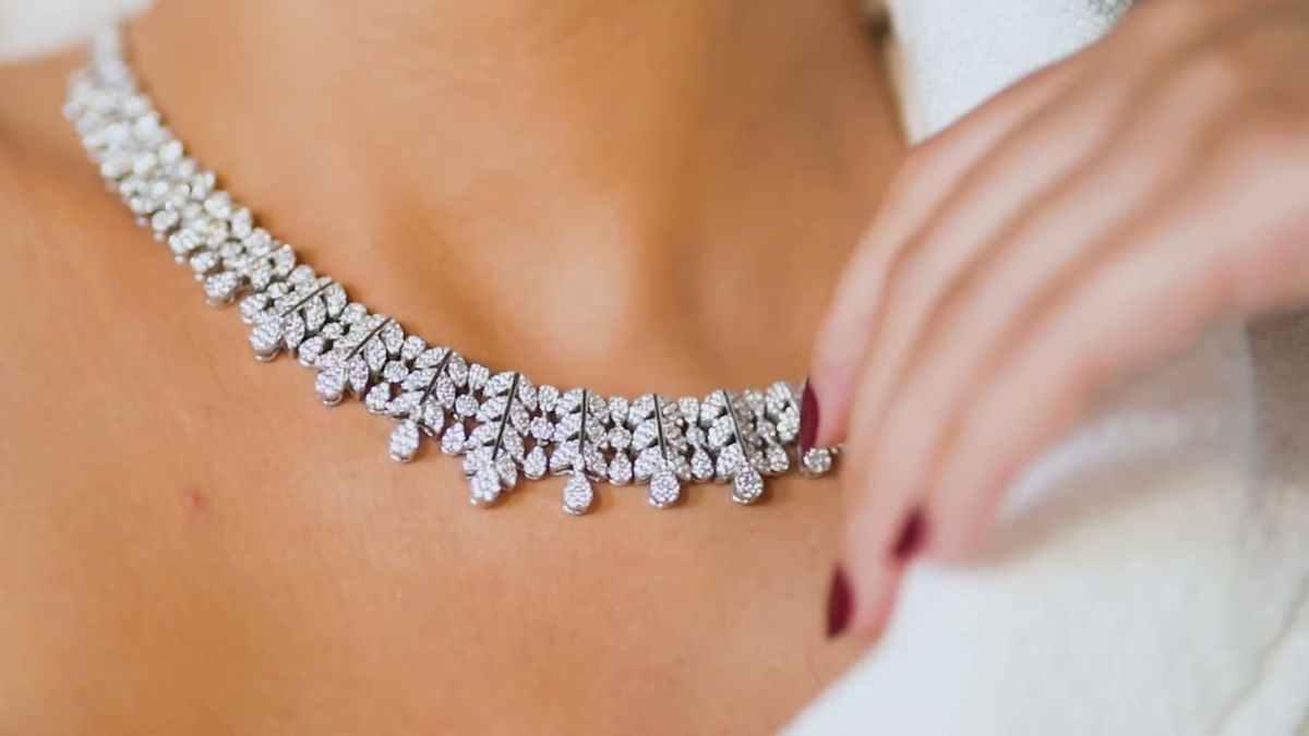 Close-up of a diamond necklace and a hand with dark nail polish