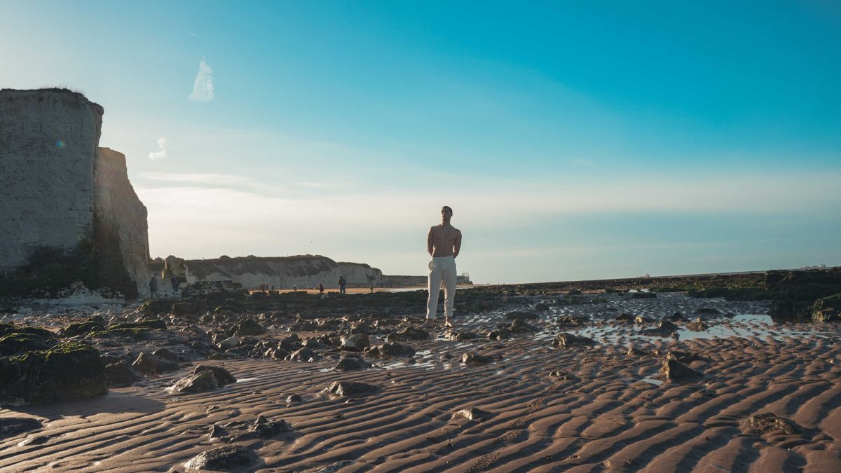 Wide view of a Kent beach at low tide with chalk stacks and a model standing on the sand