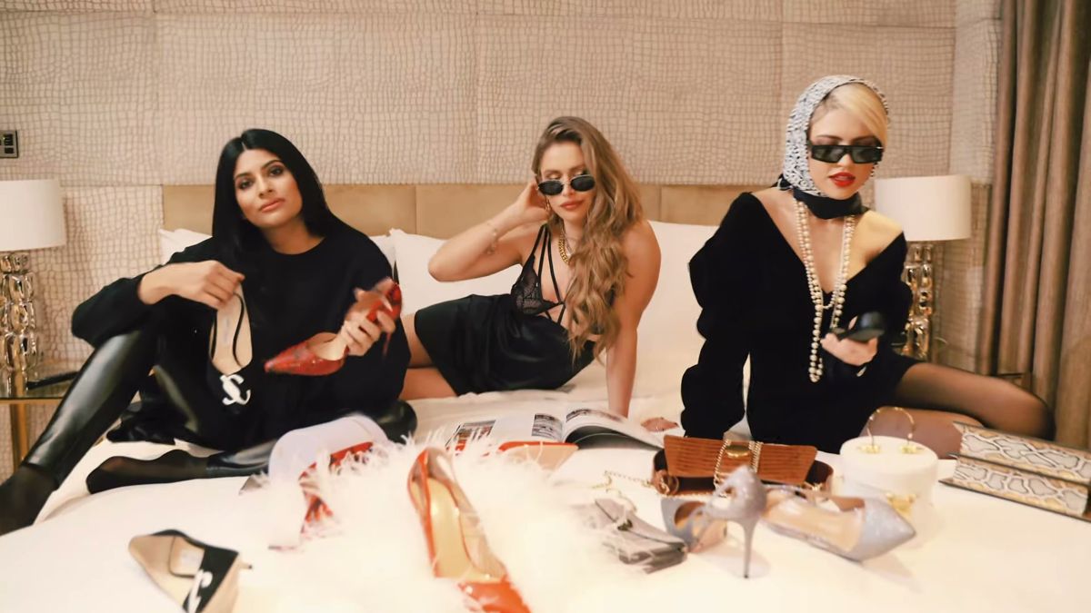 Three models on a hotel bed with shoes and bags during a fashion shoot at The Mayfair Hotel, London