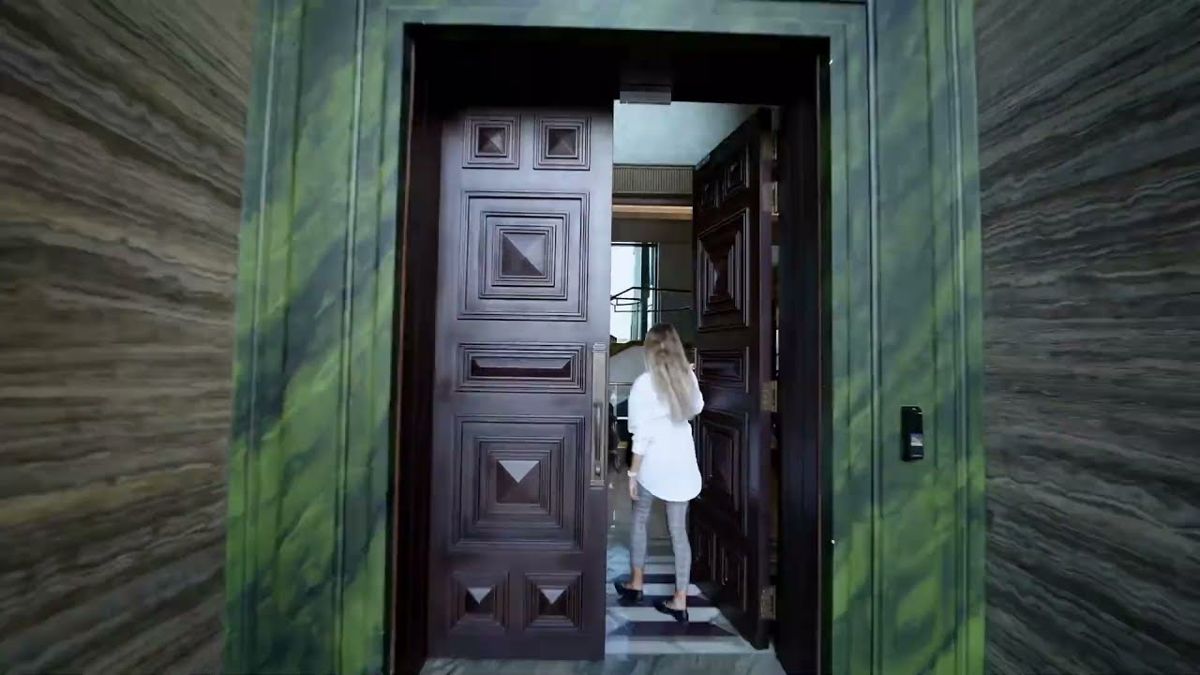 A woman opening a tall carved front door into a Dubai luxury property, an arrival shot