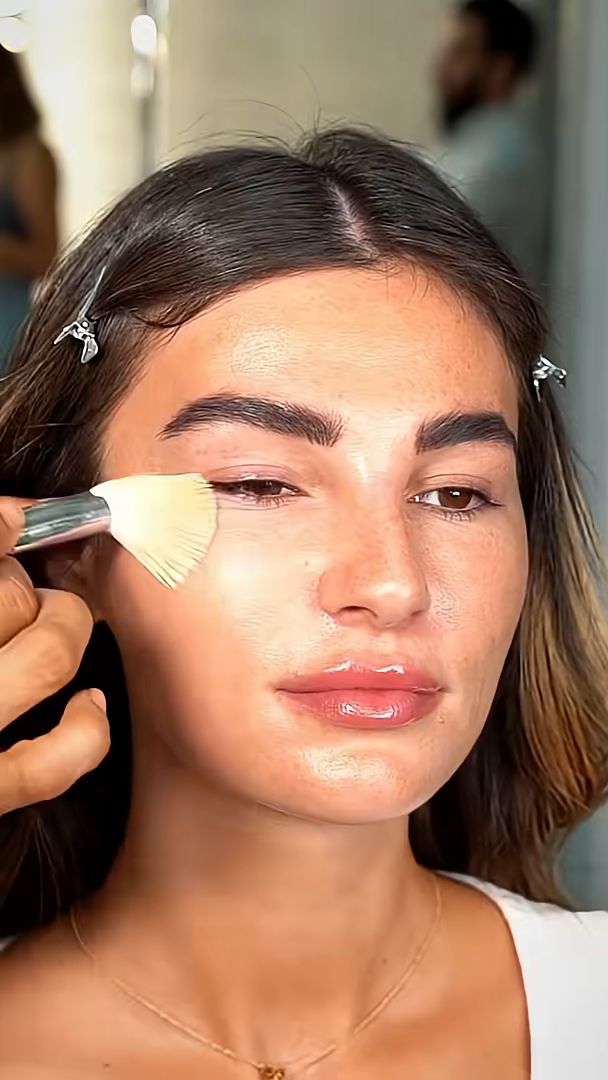 Fan brush placing highlighter on the cheekbone on glowing prepped skin