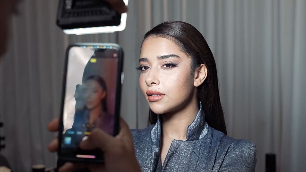 Phone capturing a finished make-up look under an LED panel backstage