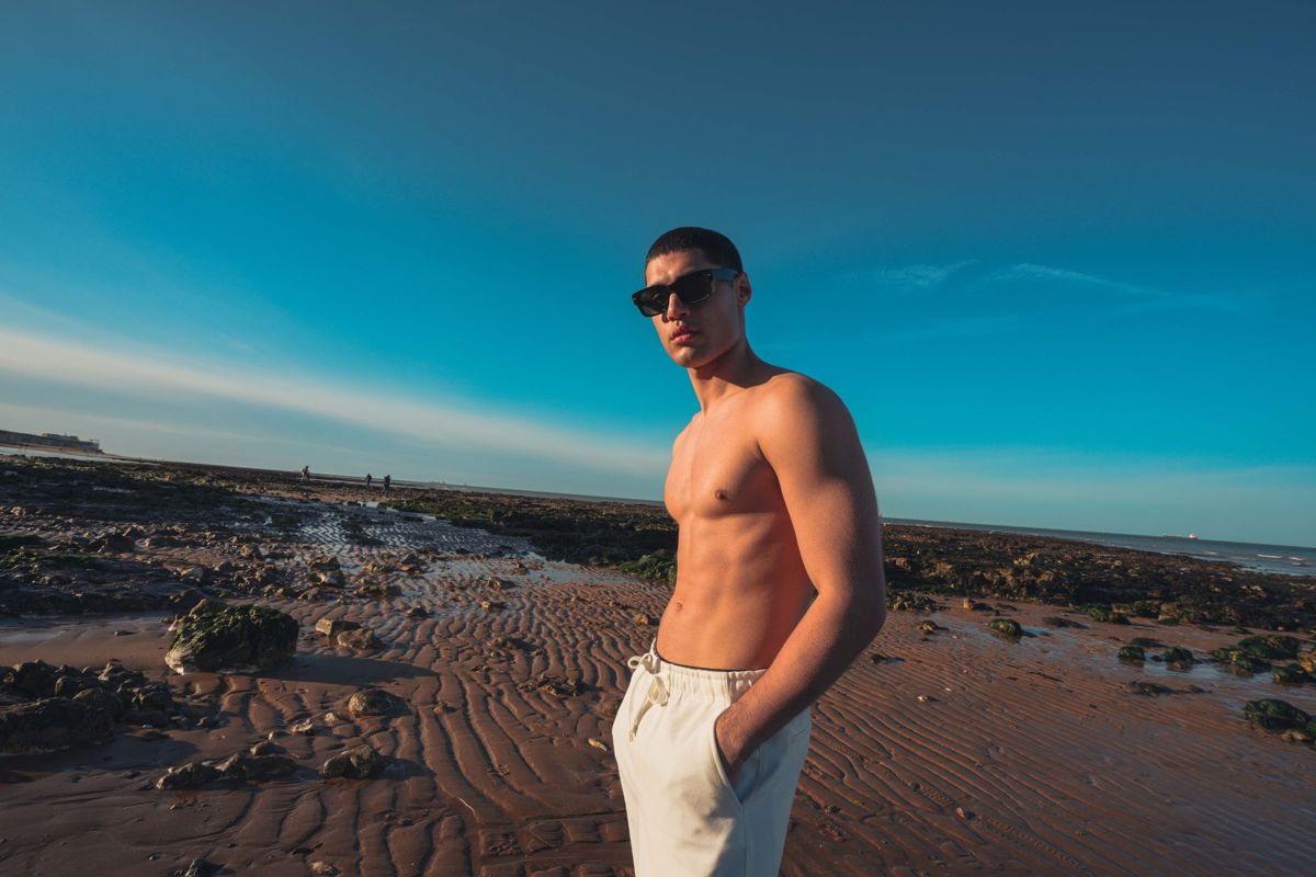 Male model in sunglasses and an open cream shirt on the Kent coast under a deep blue sky