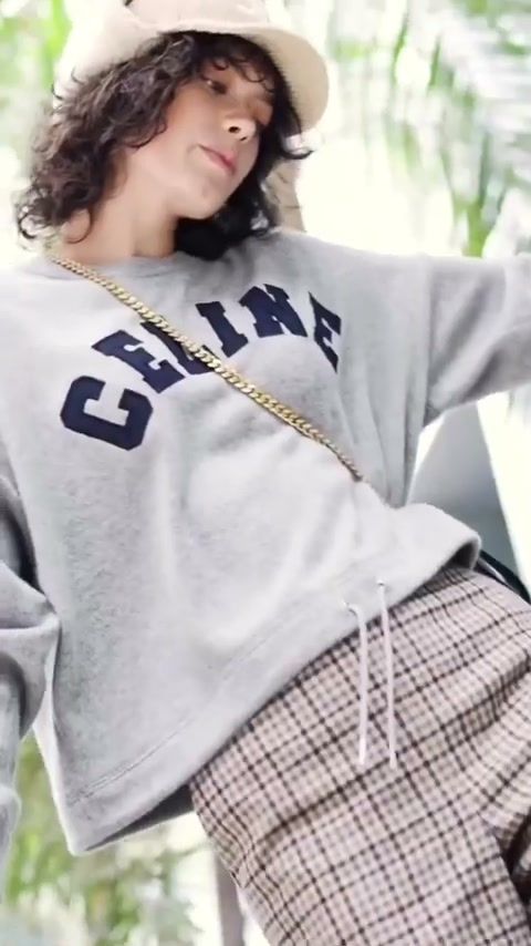 Fashion film frame: model in a logo sweatshirt and checked trousers with a shoulder bag