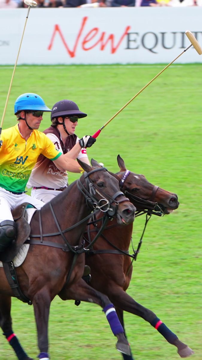 Two polo players riding shoulder to shoulder past the pitchside boards, vertical frame