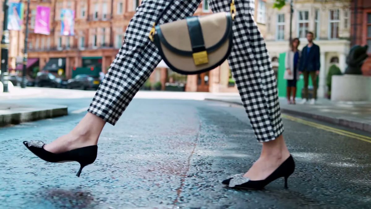 Low angle of black heels and a saddle bag mid-stride on a wet London street, Staccato