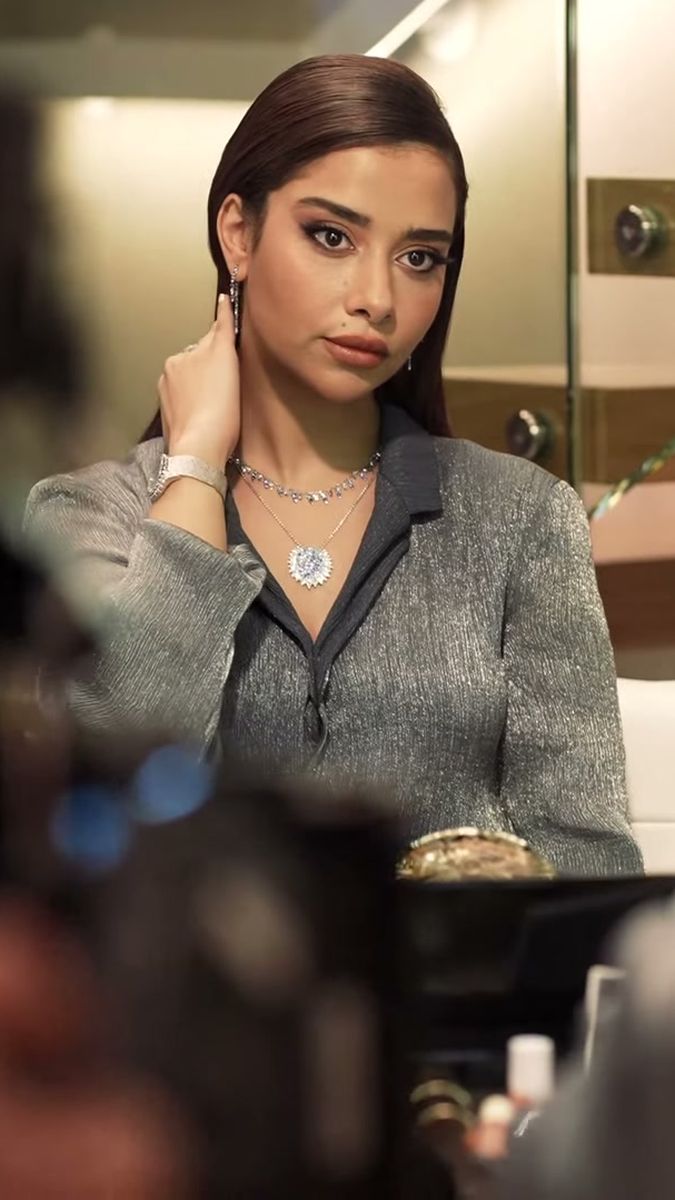 Balqees Fathi at the mirror wearing a diamond necklace and watch, camera rig in the foreground, vertical