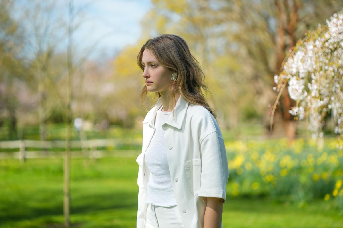Alice in the white look beside daffodils and a park fence, second look of the Linden Staub test