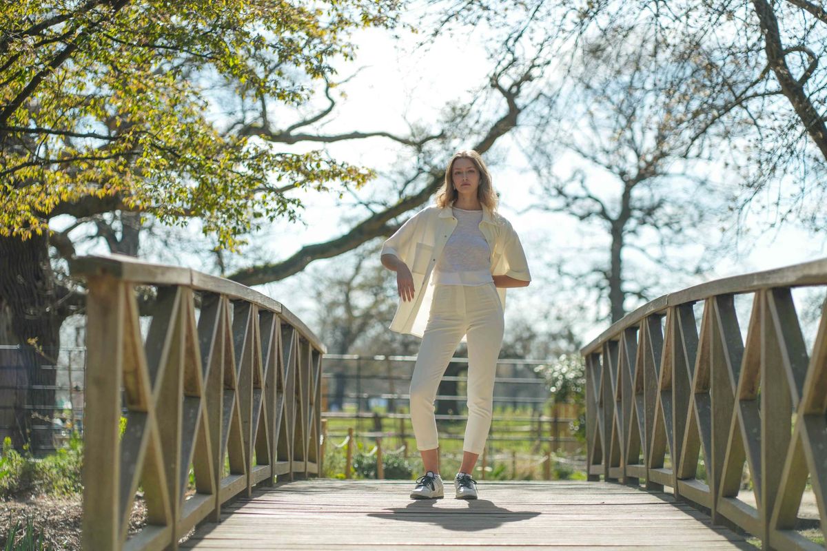 Full-length frame of Alice in white standing on a wooden footbridge, model test shoot in Richmond, London