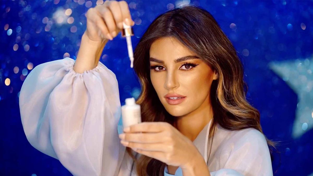 Model holding a Charlotte Tilbury serum dropper against a starry blue backdrop, Eid billboard campaign