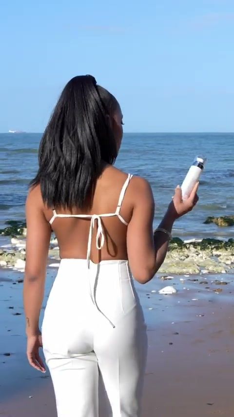 Model in white walking along the beach towards the sea holding a Seacra bottle