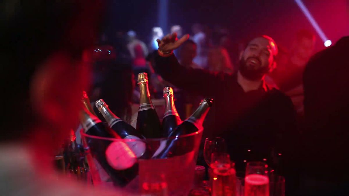 Champagne bottles in an ice bucket under red club light, with a guest celebrating behind