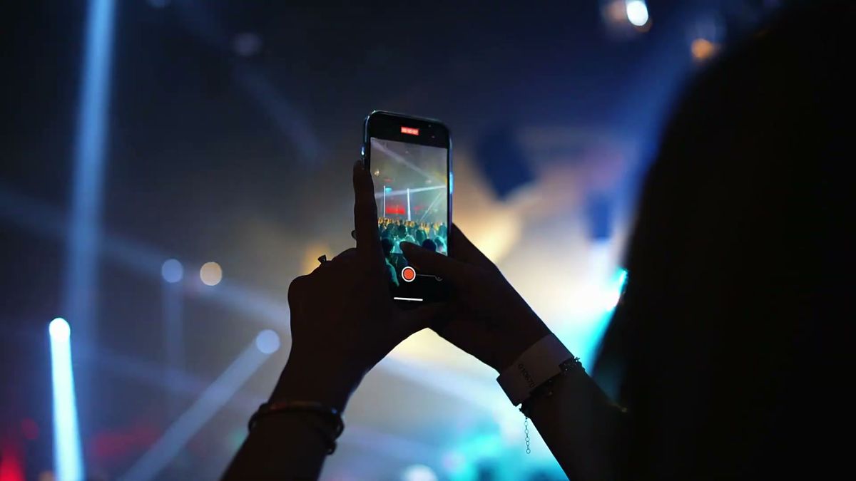A guest filming the stage on a phone through lights and haze