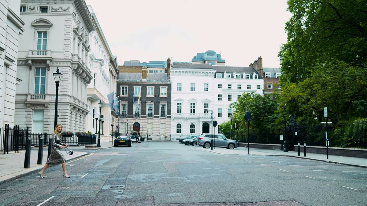 Wide shot of a white stucco London square with the model crossing the road